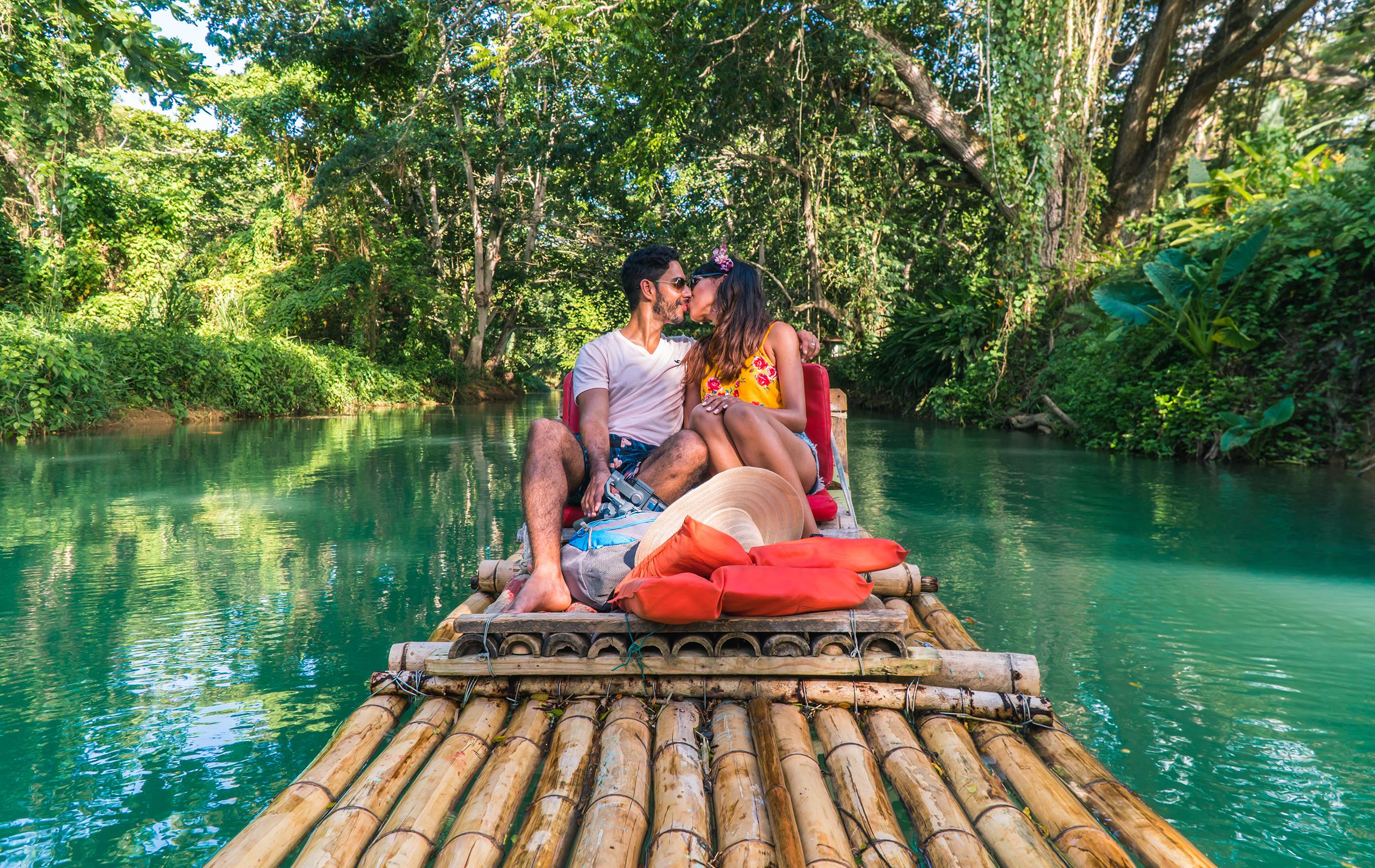 Couple kissing and taking a romantic ride down Martha Brae river, on bamboo raft. Sweet honeymoon vacation in Montego Bay, Jamaica, Caribbean.