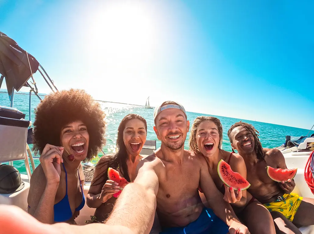 Happy friends eating watermelon while doing sea tour with sailing boat